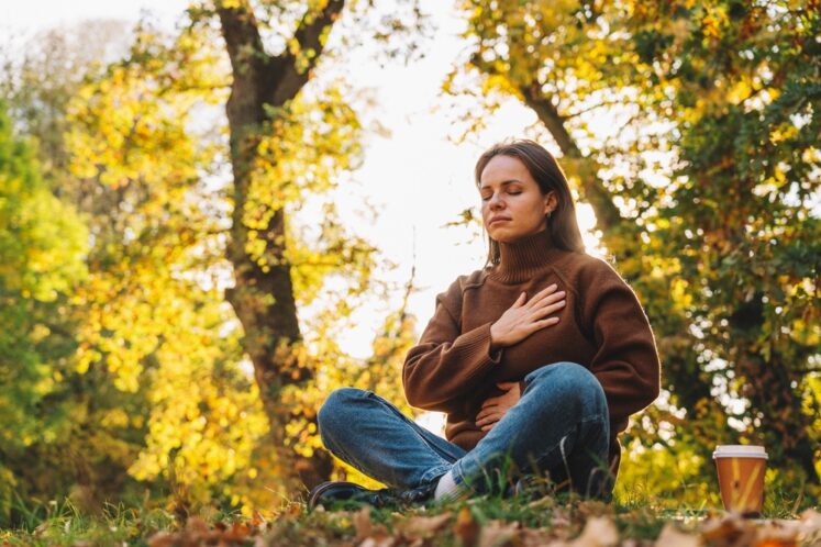 Woman practicing somatic exercises for stress relief outdoors, sitting calmly and grounded.